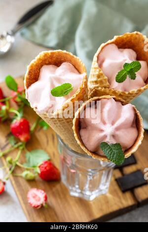 Gelato alla fragola biologico fatto in casa. Fragola di gelato in coni di waffle su un tavolo di pietra o ardesia leggera. Foto Stock