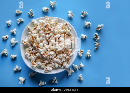 Popcorn in ciotola bianca su sfondo blu e pop corn versato senza un piatto sulla scrivania. Concetto di cibo fatto in casa Foto Stock