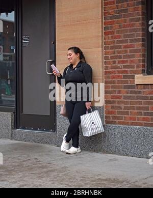 Donna che aspetta un giro usando il telefono delle cellule e tenendo una borsa da take out con il cibo dal caffè latte. St Paul Minnesota, Minnesota, Stati Uniti Foto Stock