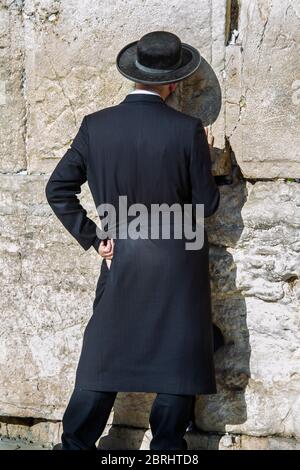 Un uomo religioso, vestito di nero, che prega al 'Wailing Wall' o al Muro Occidentale nella Città Vecchia di Gerusalemme. Pietra della Fondazione, più sacra al giudaismo, dietro il muro. Foto Stock