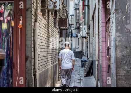 Xian / Cina - 3 agosto 2015: Uomo, membro della minoranza etnica musulmana di Hui che cammina lungo una stretta strada hutong nel quartiere musulmano di Xian, Shaanxi Provin Foto Stock