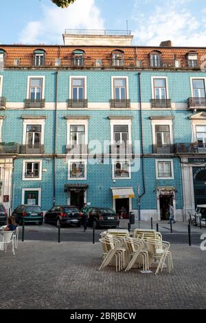 Europa, Portogallo, Lisbona. Sedie da un caffè chiuso accatastato di fronte ad un edificio blu nella vecchia Lisbona. Foto Stock