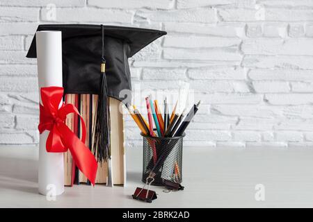 Cappellino accademico e diploma di laurea scroll e legato con nastro rosso su tavolo di legno bianco. Foto Stock