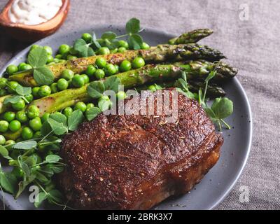 bistecca di manzo arrosto, montone con piselli verdi di asparagi su un piatto, salsa bianca Foto Stock