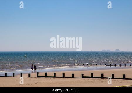 Due persone camminano lungo la spiaggia di Dymchurch, Kent. La centrale nucleare di Dungeness è visibile sullo sfondo. Foto Stock