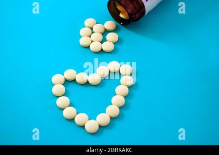 Cuore di pillole gialle su sfondo blu. Sparse otto compresse gialle e una parte di un vaso di vetro sopra di esso Foto Stock