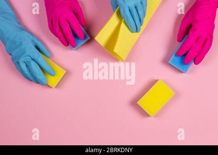 Le mani delle donne in rosa e azzurro guanti di gomma con spugne su sfondo rosa Foto Stock