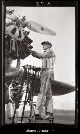 Il lavoratore addetto alla manutenzione ispeziona un aereo Ford Tri-Motor 1929. Questa vista mostra uno dei tre motori a pistoni radiali di questo storico velivolo da trasporto. Immagine da 2.5 x 4.25 pollici negativo. Foto Stock
