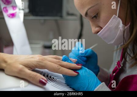 Concetto: Cura personale, manicure. Manicurista che lavora. Giovane ragazza che fa lavoro di unghia sulle mani di donna adulta. Vista laterale. Lavori su vernice acrilica per unghie. Foto Stock