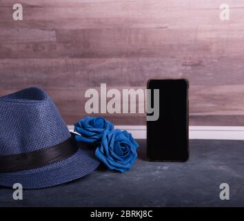 Omaggio accessorio uomo per il Father's Day o l'anniversario su sfondo tavola di legno, rose blu, cappello e telefono cellulare. Foto Stock