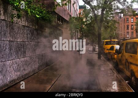 New York City, USA, 2019 maggio, pedonale con un ombrello che passa accanto a una bocchetta di ventilazione e alcuni taxi parcheggiati in una giornata di pioggia Foto Stock