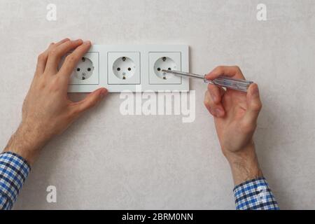 Mano dell'elettricista che usa un cacciavite per tester di fase per riparare la presa a muro Foto Stock