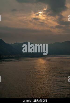 Guandukou, Hubei, Cina - 7 maggio 2010: Gola di WU nel fiume Yangtze. Il sole della mattina presto prova a rompere attraverso la linea dorata vivente densa del paesaggio nuvoloso su scuro Foto Stock