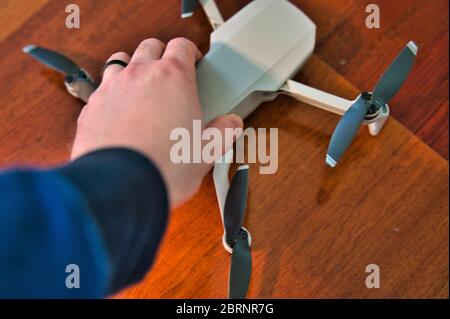 Drone con tenuta a mano con ponte in legno visibile sullo sfondo. Mano bianca dell'uomo che afferra il piccolo drone volante preparandolo a decolli. Foto Stock