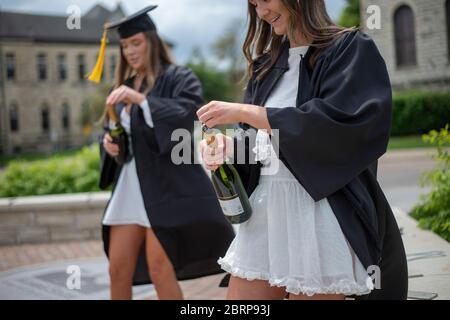 Manhattan, Kansas, Stati Uniti. 16 maggio 2020. Kansas state University Speech laureato in patologia, KAITLYN KUHL, destra, e laureato in biologia, AUTUNNO WRANOSKY, sinistra, smalva bottiglie di champagne per una foto di laurea di fronte alla Anderson Hall. Sabato è stato il giorno della laurea alla KSU, tuttavia le classi e le lauree sono state annullate a causa della pandemia COVID-19. Credit: Luke Townsend/ZUMA Wire/Alamy Live News Foto Stock