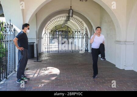 San Gabriel, California, Stati Uniti. 20 Maggio 2020. L'ospite della TV Joey Zhou è istruito dall'ex sprinter olimpico Feng li in esercizi di riscaldamento come parte del 'programma di idoneità pandemico' di Joey Zhou per aiutare gli altri a ottenere l'esercitazione mentre rimangono sicuri durante la pandemia di Covid-19 al Playhouse della missione di San Gabriel a San Gabriel, California. Feng li ha rappresentato la Cina ai Giochi Olimpici estivi del 1988 e ora vive negli Stati Uniti. Il San Gabriel Mission Playhouse è stato costruito nel 1927 ed è un luogo storico per le arti dello spettacolo. Credito: Sheri Determan Foto Stock