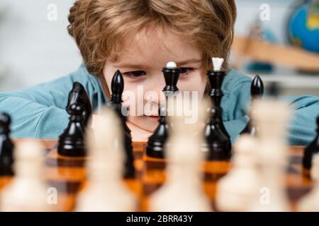 Ragazzino intelligente che pensa agli scacchi. Bambini sviluppo precoce. Figlio sta giocando a scacchi e sorridendo a casa. Primo piano ritratto, volto divertente Foto Stock