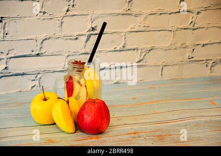 Le mele mature gialle e rosse si trovano vicino a un bicchiere di succo di ghiaccio su un tavolo di legno. Primo piano. Foto Stock