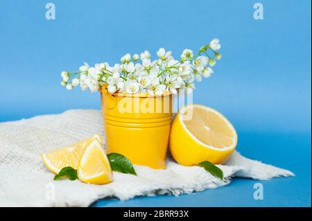 Fiori bianchi di ciliegia in un decoro di metallo giallo, fette di limone e un limone intero con foglie di menta su un tovagliolo di cialda di cotone grigio su una ba blu Foto Stock