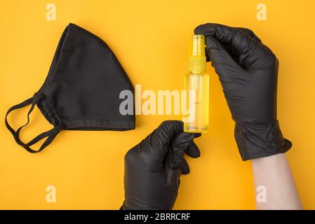 Sicurezza durante il concetto di Coronavirus. In alto, vista dall'alto, foto delle mani della donna in guanti che tengono una bottiglia di disinfettante per le mani con una maschera da parte Foto Stock