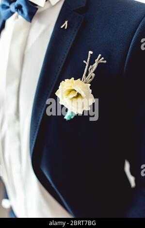 Dettagli di abiti da sposa maschile. Bel boutonniere con pinning sull'uomo in tuta blu, camicia bianca e cravatta blu. Foto Stock