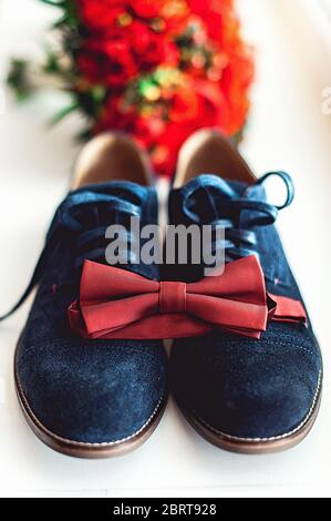 Primo piano degli accessori uomo moderno. Cravatta di fiocco di ciliegio, scarpa blu in pelle e bouquet rosso di nozze su un tappeto. Foto Stock