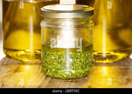 pesto di basilico fatto a mano in un vaso di vetro vicino ad alcune bottiglie di olio Foto Stock