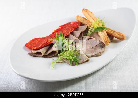 Piatto di carne affumicato freddo con costolette di maiale, prosciutto, salame e bastoncini di pane su fondo di legno bianco. Dalla vista dall'alto Foto Stock