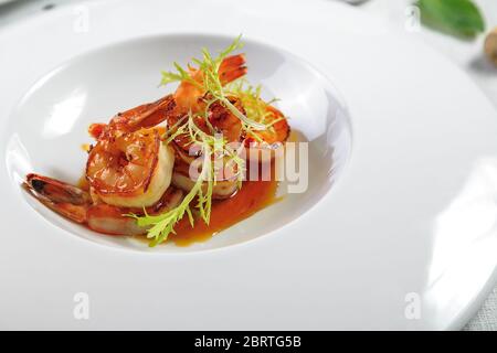 Gamberi alla griglia in piatto bianco con limone e spezie su sfondo grigio vintage, vista dall'alto, spazio copia. Tavolo da cucina in pietra con cena a base di pesce. S Foto Stock