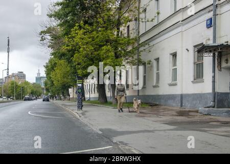 Mosca, Russia. 21 maggio 2020. Una giovane ragazza in una maschera protettiva cammina con un cane sul marciapiede lungo la strada in città in una giornata nuvolosa. Animali domestici d Foto Stock