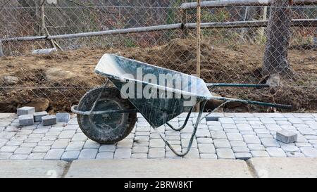 Un vecchio carriola verde metallico con una ruota e maniglie si trova in un cantiere. Dispositivo per il trasporto di merci. È costituito da un cargo bo Foto Stock