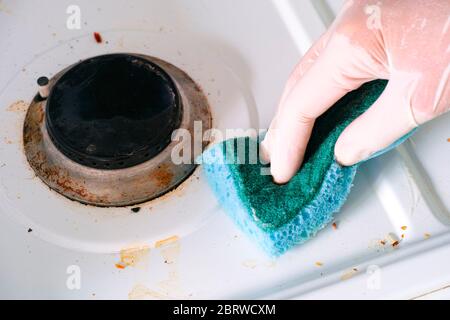 Donna mano in guanto con spugna pulizia stufa a gas sporco. Primo piano Foto Stock