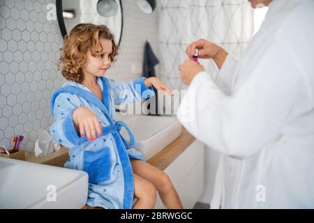 Una bambina carina con la madre in bagno in casa, dipingendo unghie. Foto Stock