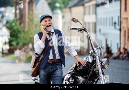 Un uomo d'affari senior con moto in città, utilizzando smartphone. Foto Stock