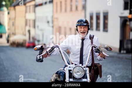 Un uomo d'affari anziano con moto in città, guardando la macchina fotografica. Foto Stock