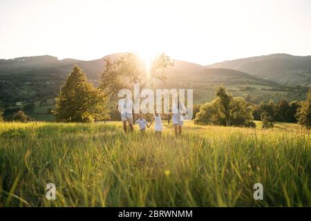 Famiglia giovane con due bambini piccoli che camminano sui prati all'aperto al tramonto. Foto Stock