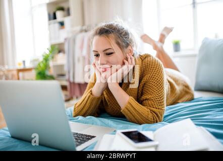 Giovane donna con computer portatile sdraiato sul letto in casa, rilassante. Foto Stock