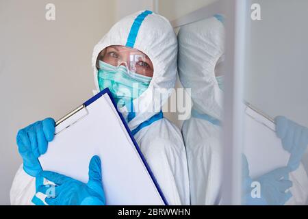 Scout di contenimento o personale infermieristico in abbigliamento protettivo con lista visitatori per il monitoraggio dei contatti a causa di pandemia di coronavirus Foto Stock