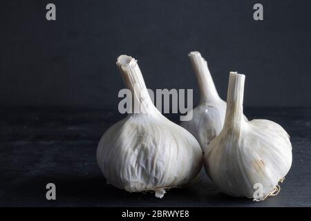 tre teste di aglio raggruppate sul lato destro su sfondo nero. cibo scuro Foto Stock