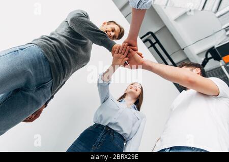 Vista dall'angolo basso dei colleghi sorridenti che tengono le mani in ufficio Foto Stock