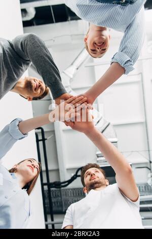 Vista dal basso di colleghi sorridenti che tengono le mani in ufficio Foto Stock