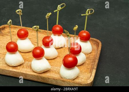 polpette di mozzarella con pomodori ciliegini su spiedini, tartine su fondo nero, formaggio con verdure Foto Stock