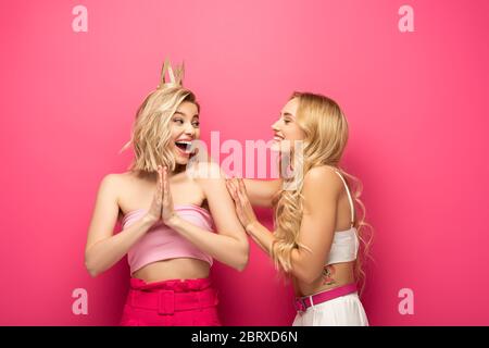 Ragazza sorridente che guarda un amico blonde eccitato in corona su sfondo rosa Foto Stock