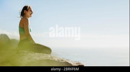 Donna sana seduta sulla scogliera che guarda la vista. Donna escursionista riposante sulla cima della montagna. Foto Stock