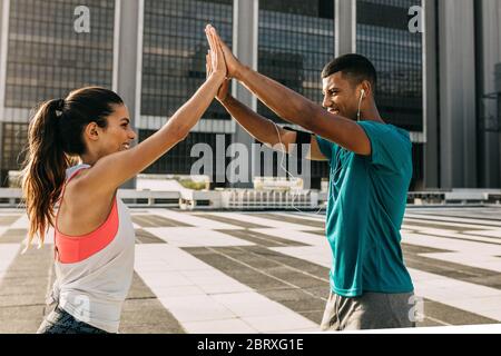 Uomo e donna sportivi che si danno a vicenda un alto cinque mentre si esercita all'aperto. Coppia che si danno un cinque alto durante il loro allenamento in città. Foto Stock