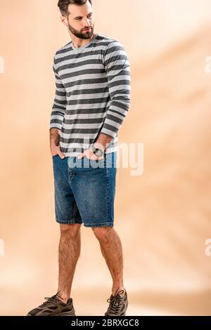 bell'uomo con bearded che si posa in felpa a righe sul beige Foto Stock