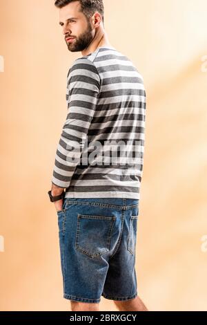 bell'uomo con bearded che si posa in felpa a righe sul beige Foto Stock