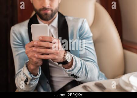 vista ritagliata di un uomo elegante che chiacchiera sullo smartphone mentre viaggi in aereo privato Foto Stock