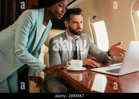 uomo d'affari serio che punta con il dito contro il laptop vicino afroamericano imprenditore Foto Stock