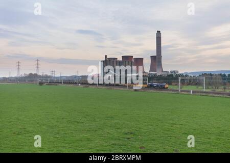 GB Railroad classe 66 locomotiva che passa per la centrale elettrica di Rugley con un treno merci che trasporta materiali per la rete ferroviaria Foto Stock